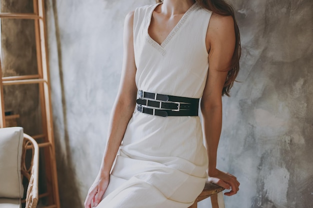 Photo a slim girl in a white dress tries on a belt with black leather