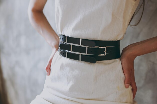 A slim girl in a white dress tries on a belt with black leather