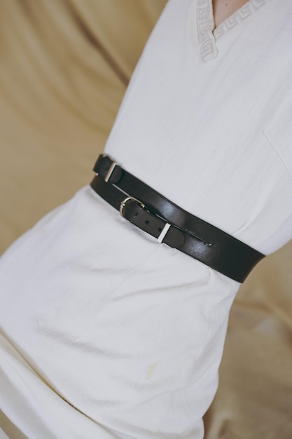 A slim girl in a white dress tries on a belt with black leather