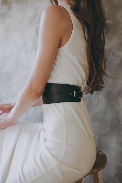 A slim girl in a white dress tries on a belt with black leather