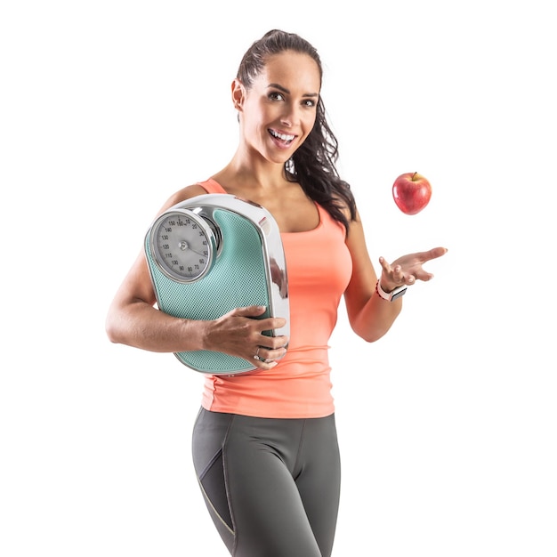 Slim and goodlooking brunette tosses an apple and holds weighing scale in her other hand