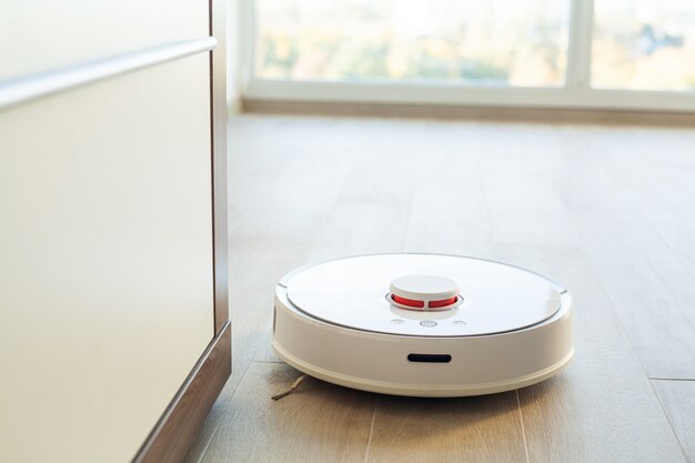 Slim huis. Stofzuigerrobot draait op houten vloer in een woonkamer