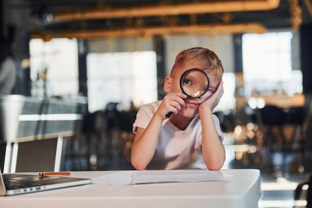 Foto slim kind in vrijetijdskleding met laptop op tafel veel plezier met vergrootglas