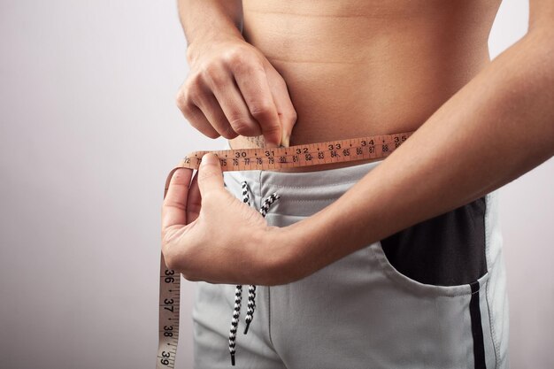 Slim man measuring belly fat with a tape studio shot