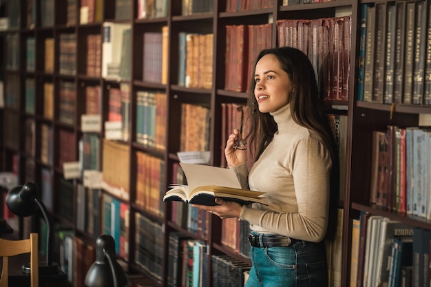 Slim meisje met een wit overhemd in de buurt van de planken in de bibliotheek