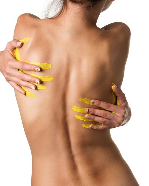 Slim naked young woman with tattoo standing backwards with yellow fingerprints on her back