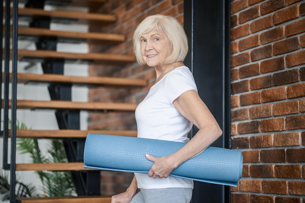 Slim senior woman with yoga mat in hands