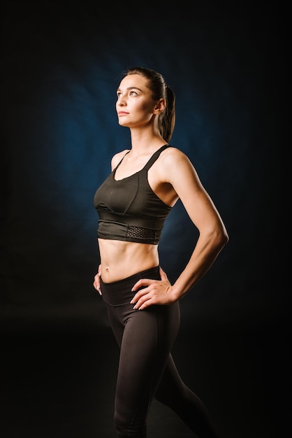 Slim sport woman doing exercises on the black studio background
