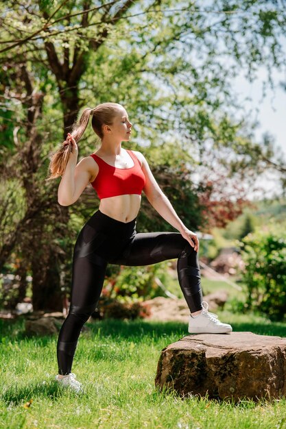 Slim sporty young woman in sportsweat posing or resting outdoors in the park