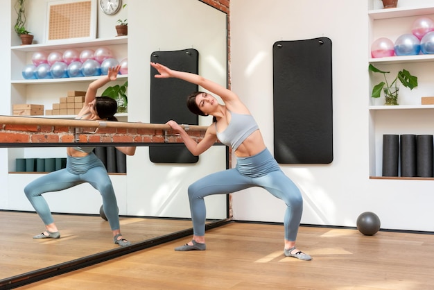 Slim woman doing Plie squat near barre in studio