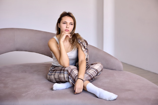 Slim woman in home suit sits on bed in bedroom