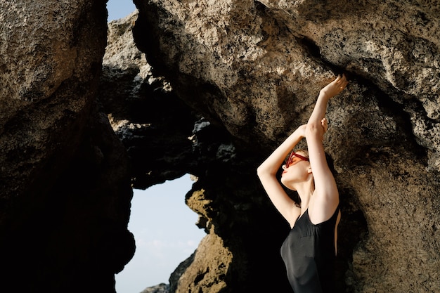 사진 바위 패션 스타일을 배경으로 바다에서 포즈를 취하는 검은 수영복을 입은 슬림 여성
