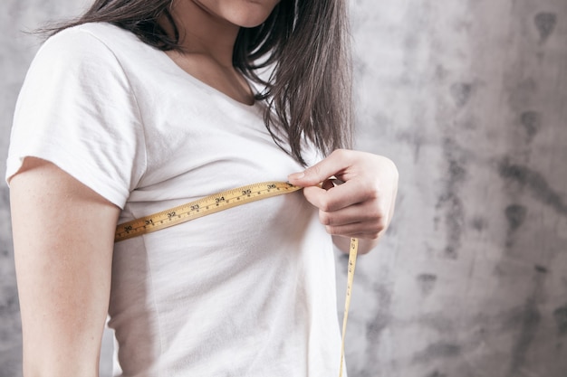 Slim woman measures her breast with a measuring tape