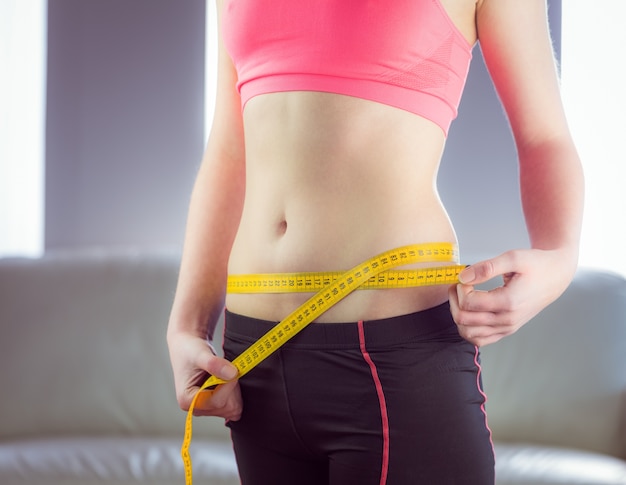 Slim woman measuring waist with tape measure