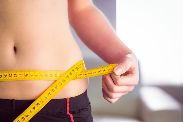 Slim woman measuring waist with tape measure