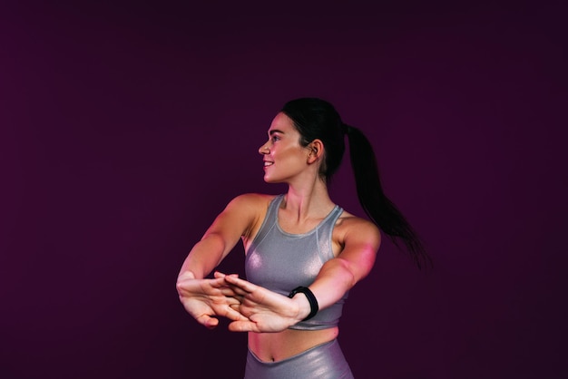 Slim woman in silver fitness wear doing warmingup exercises against a magenta background