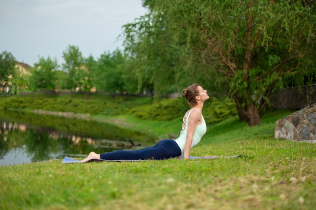 Slim young brunette yogi performs yoga exercises on the green grass