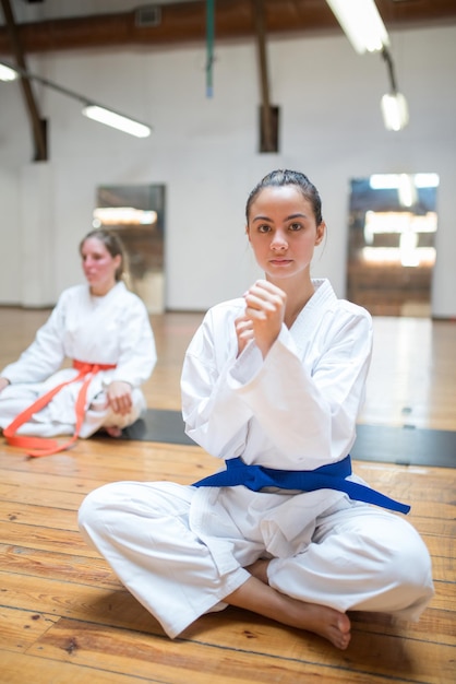 Slim young Caucasian karate girl with her fists up ready for class. Sporty female karateka sitting in karate position. Sports, martial arts, healthy lifestyle concept