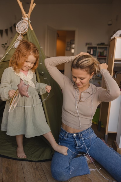 Slim young caucasian woman in casual clothes sits on floor with redhaired baby girl in room Family concept