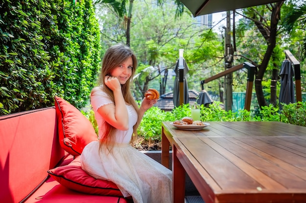 Slim Young Woman Enjoy Eating Fresh Bakery Food. Happy Female Take Plate with Delicious Pastry, Waffles and Buns. Smiling Girl with Long Hair Eat Sweet Tasty Buns in Outdoor Cafe, looking at Camera