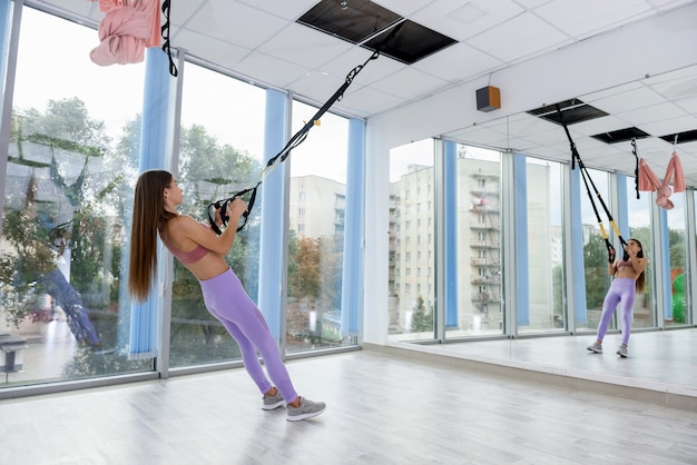 Slim young woman exercising working out with TRX straps at the gym. Fitness workout for female body