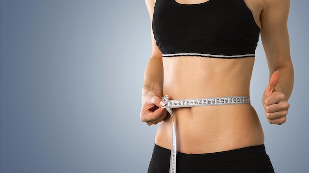 Slim young woman measuring her thin waist with a tape measure, close up