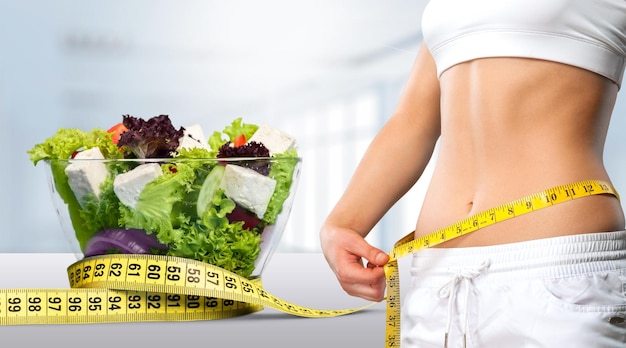 Slim young woman measuring her thin waist with a tape measure, close up