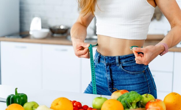 Photo slim young woman measuring her thin waist with tape measure closeup view