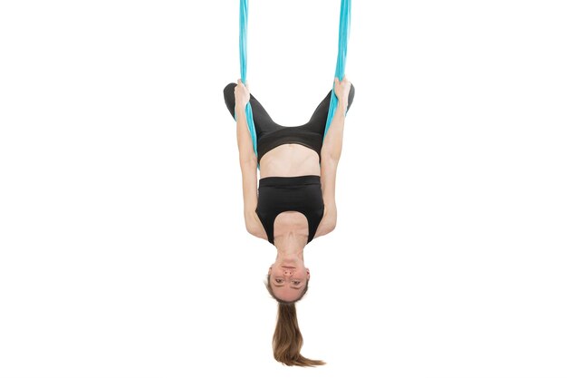 Slim young woman practices inverted pose asana on hammock Fly yoga or aerial gymnastics Girl hangs upside down