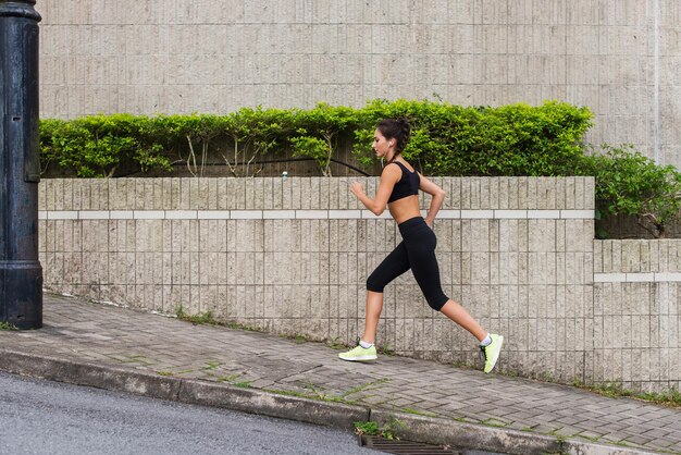 Slim young woman running uphill on sidewalk of city street Female athlete training outside