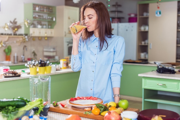 新鮮なジュースを飲みながらキッチンに立っているスリムな若い女性