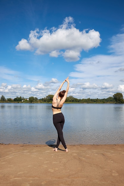 写真 湖の近くの砂の上に伸びるスリムな若い女性。