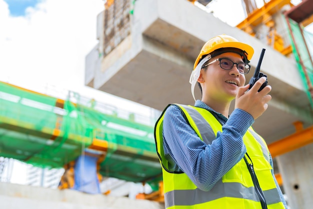 Slimme aziatische ingenieursmanager met veiligheidsuniform die de bouw van de site controleert met een achtergrond van staal en betonstructuur