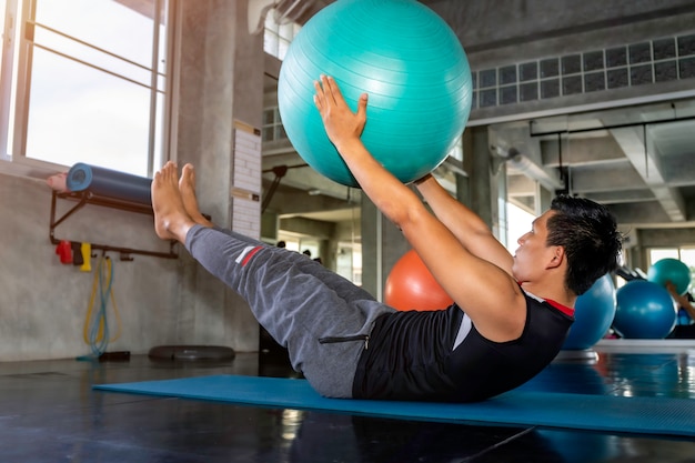 Slimme aziatische man in sportkleding training buikspieren met bal gym op fitness.