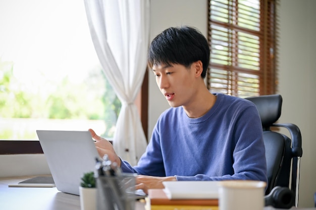 Slimme Aziatische mannelijke kantoormedewerker die laptop gebruikt en een online vergadering heeft met zijn team