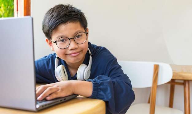 Slimme Aziatische studentenjongen met een bril die lacht, hij gebruikt computer-laptop internet op sociale netwerken