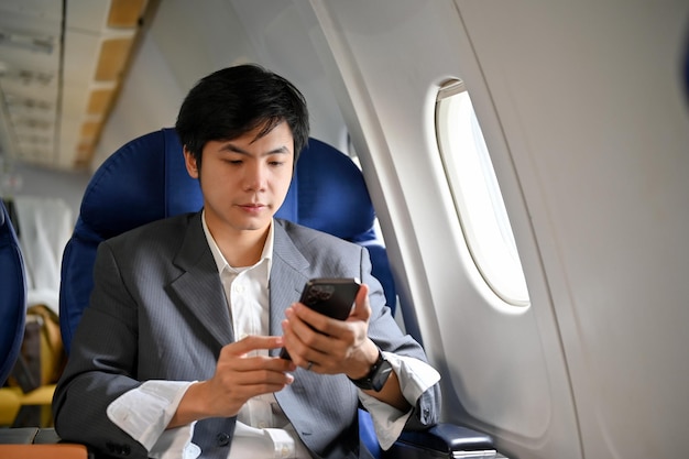 Slimme Aziatische zakenman die zijn smartphone gebruikt tijdens de vlucht op zijn privéjet