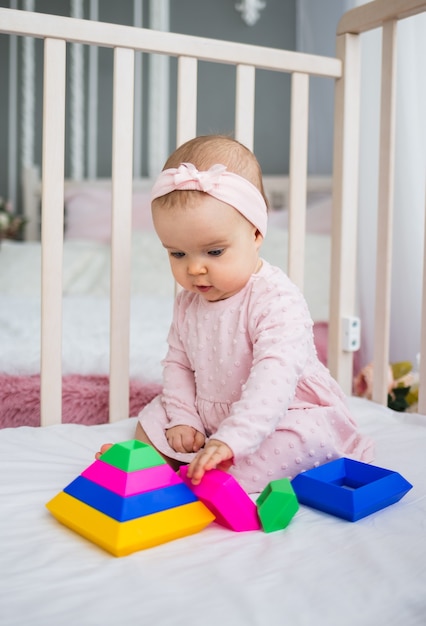 Slimme babymeisje verzamelt een piramide in de wieg in de kamer. ontwikkeling van het vroege kind