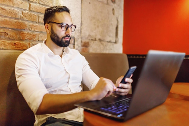 Slimme bebaarde man aan het werk met laptop tijdens het drinken van koffie in de werkruimte