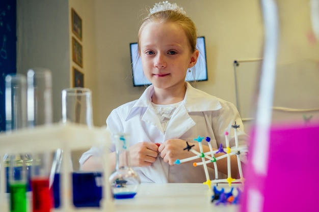 slimme blonde schoolmeisje scheikundige in brillen en witte medische jurk maken van wetenschappelijke experimenten chemie, verschillende chemische oplossingen mengen in laboratorium klas