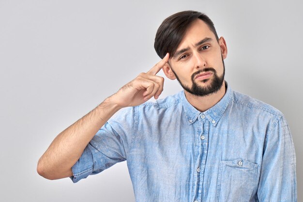 Slimme brunette man in casual aanrakingen hoofd denkt dat twijfels een beslissing nemen geïsoleerd op blauwe studio achtergrond