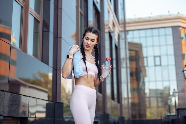 Slimme fit vrouw met een fles water en een handdoek op haar schouder in de stad Gezonde levensstijl Fitness concept