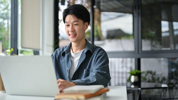 Slimme jonge Aziatische man die naar het laptopscherm kijkt met behulp van een laptop op afstand die in het café werkt