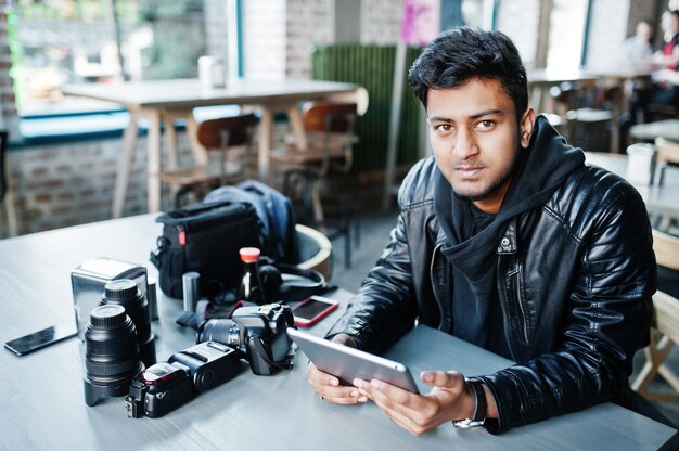 Slimme jonge Aziatische mensenfotograaf die met tablet werkt tijdens het zitten bij koffie