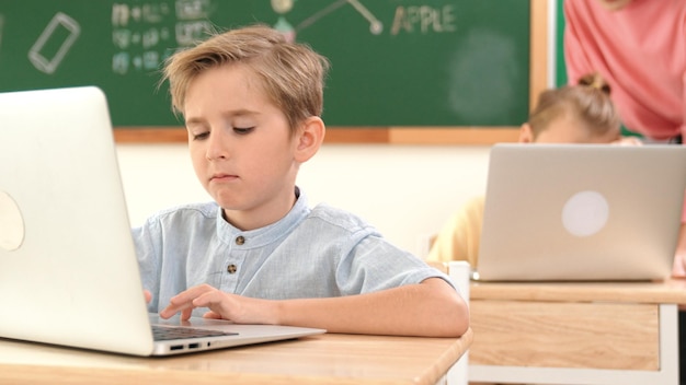Slimme jongen die aan een laptop werkt terwijl verschillende kinderen een systeem programmeren Pedagogie