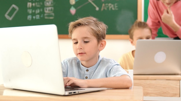 Slimme jongen die aan een laptop werkt terwijl verschillende kinderen systeempedagogie programmeren