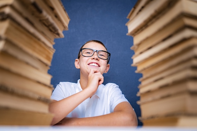 Slimme jongen in glazen zitten tussen twee stapels boeken en bedachtzaam opzoeken.