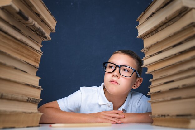 Slimme jongen in glazen zitten tussen twee stapels boeken en bedachtzaam wegkijken