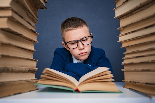 Slimme jongen in glazen zitten tussen twee stapels boeken en boek zorgvuldig lezen