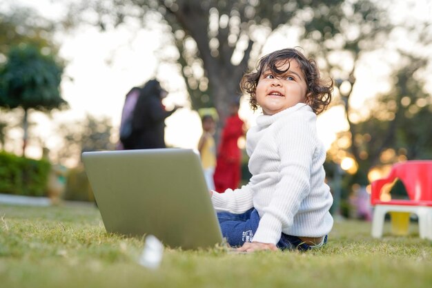 Slimme kleine jongen die in de tuin speelt terwijl hij een laptop gebruikt op het verzekeringsconcept van weidehuis